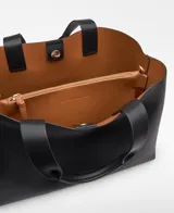 Bolso shopper horizontal negro de piel sintética, con dos compartimentos, cierre magnético y bolsillo interior con cremallera. Cuenta con asa de mano y correa larga regulable y extraíble, además del logo grabado en el frente.