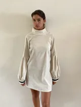 Vestido corto de color manteca con cuello alto, mangas largas abullonadas y puños con detalle de rayas en contraste.