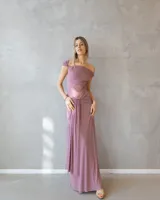 Vestido largo color malva con escote barco, cuerpo ajustado y falda fluida con detalle de drapeado y fruncido en la cintura.