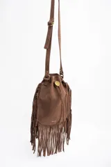 Cartera tipo bucket color marrón, confeccionada en material sintético con acabado gamuzado. Presenta flecos largos en los laterales y la base, cierre mediante cordón ajustable y correa larga regulable para llevar al hombro o cruzada.