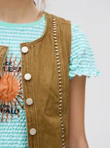 Chaleco de denim liviano con cierre frontal de botones metálicos, detalle de apliques metálicos verticales y ruedo con terminación desflecada.