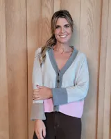 Cardigan de lana lambswool con cuello en V y cierre frontal de botones. Presenta un diseño de bloques de color que combina tonos beige, gris, rosa y marrón en los puños, con un ajuste holgado.