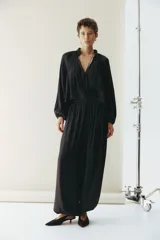 Blusa oversize corta color negro, confeccionada en tejido brillante. Presenta cuello nido de abeja con frunces y escote en V profundo, mangas globo largas de corte raglán y puños elásticos.