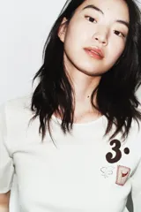 Camiseta de manga corta color blanco, con cuello redondo y bajo recto. Presenta un pequeño bordado y estampado en el pecho, incluyendo el número "3." y un pequeño cuadrado con un corazón.