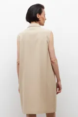 Vestido corto color beige, sin mangas, con cuello camisero, cierre frontal con cordones cruzados y múltiples bolsillos con cierre.