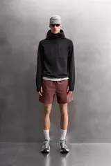 Pantalones cortos deportivos color marrón rojizo, confeccionados en tejido técnico ligero y elástico. Presentan cintura elástica ajustable con cordón interior, bolsillos frontales y un bolsillo trasero con cierre de cremallera. Los laterales tienen perforaciones para transpirabilidad y aberturas laterales en el bajo.