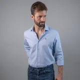 Camisa sport de hombre color celeste, confeccionada en 100% algodón, con cuello clásico, manga larga y puños abotonados. Presenta un logo bordado en el pecho.