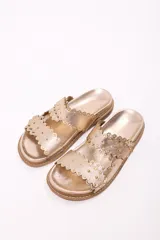 Sandalia tipo mule de mujer, color dorado metalizado, con dos tiras anchas superpuestas con borde festoneado y tachas doradas. La suela es gruesa y de color marrón claro.