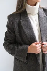 Blazer de corte sastrero en color gris oscuro con textura jaspeada. Presenta solapas clásicas, cierre frontal de doble botonadura y un bolsillo superior con detalle de pañuelo decorativo.
