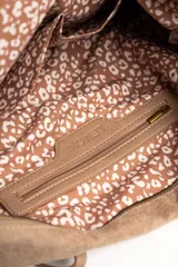 Bolso tipo shopper de gamuza vegana color tostado, con doble asa larga para hombro y cierre superior. Cuenta con una pequeña placa metálica con el logo de la marca en la parte frontal.
