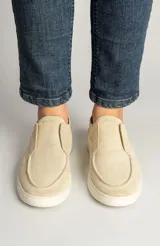 Zapatillas de gamuza color arena, diseño sin cordones estilo slip-on, con costuras decorativas en el empeine y suela de goma blanca.