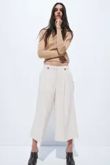 Pantalón sastrero cropped de tiro alto, color beige, con piernas amplias, pliegues frontales, bolsillos al bies y trabillas en la cintura con detalles de botones.