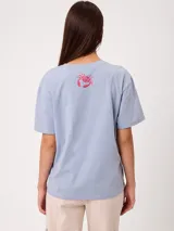 Remera celeste de corte holgado, con cuello redondo, manga corta y estampado frontal colorido de temática costera.