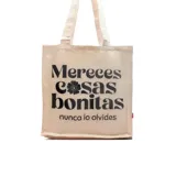 Tote bag de tela color beige con estampado frontal en color negro que incluye la frase 'Mereces cosas bonitas, nunca lo olvides'. Cuenta con dos asas largas para llevar al hombro.