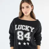 Buzo de felpa color negro con cuello redondo amplio y mangas largas. Presenta un estampado frontal en color blanco con la palabra 'LUCKY', el número '84' y tres estrellas.