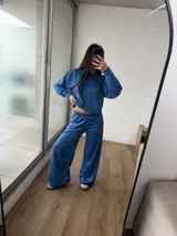 Conjunto deportivo de dos piezas color azul, compuesto por un buzo de cuello redondo y mangas largas, y un pantalón de corte ancho con cintura elástica. El buzo presenta un diseño reversible con costuras visibles.