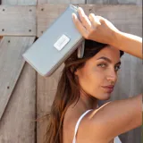 Billetera larga con cierre perimetral, confeccionada en material sintético con estampado botánico de flores silvestres sobre fondo claro. Cuenta con múltiples compartimentos internos para tarjetas, visor para documentos y un bolsillo interno con cierre. Incluye una correa de mano extraíble.