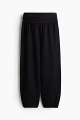 Pantalón negro de corte holgado en tejido de punto con efecto arrugado. Presenta una cintura ancha fruncida con elástico oculto y piernas globo con bajos elásticos.