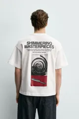 Camiseta de corte relajado, cuello redondo y manga corta. Presenta un pequeño estampado de texto en el pecho y un estampado gráfico de mayor tamaño en la espalda.