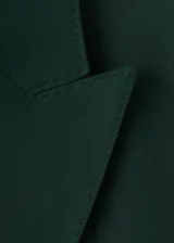 Blazer de corte recto y diseño estructurado, confeccionado en tejido mezcla de lana color verde oscuro. Presenta cuello con solapas de muesca, cierre frontal de doble botonadura, bolsillos de solapa laterales y bolsillo de ribete en el pecho. Incluye forro interior y mangas largas con puños abotonados.