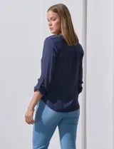 Blusa blanca de gasa marca Zac & Rachel, con cuello a la base, escote en V, abertura central con botones, bolsillo aplicado en el pecho y mangas largas regulables con presilla y botón. Tiene terminación opcional de nudo en el ruedo.