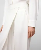 Pantalón blanco de pierna ancha y recta, estilo pareo, con cruce frontal envolvente y cintura elástica en la espalda. Presenta bolsillos laterales y falsos bolsillos traseros.