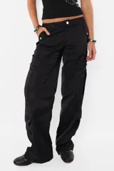 Pantalón cargo negro de corte recto y tiro bajo, con recortes y múltiples bolsillos laterales y traseros con tapa y botón a presión. Cierre frontal con cremallera de nylon y botón personalizado.