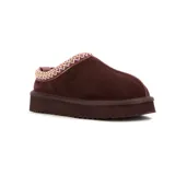 Pantufla tipo mule de cuero gamuzado color marrón, con interior de peluche y detalle de costura decorativa trenzada en el borde superior. Cuenta con una suela de plataforma dentada de goma.