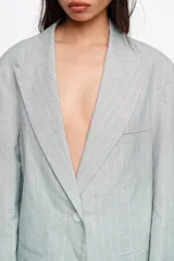Chaqueta gris claro con sutiles rayas verticales rosadas, corte oversize, solapas amplias y cierre frontal de un botón.