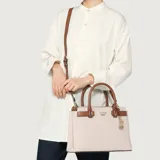 Cartera tipo satchel Guess modelo Reena, confeccionada en lona color beige con detalles en cuero sintético marrón. Cuenta con doble asa superior, correa ajustable y extraíble, cierre superior y dije metálico colgante con el logo de la marca.