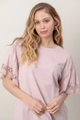 Remera de algodón color rosado, de corte holgado, con cuello redondo y mangas cortas amplias con detalles de broderie en los puños.