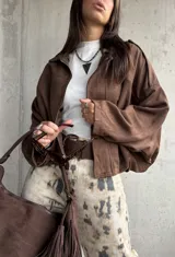 Campera tipo bomber de gamuza color chocolate, con diseño oversize, mangas amplias y apliques decorativos en los hombros. Cuenta con cierre frontal y forro interior.