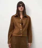 Chaqueta de corte recto confeccionada en suede sintético color marrón. Presenta cuello estilo camisa, cierre frontal con botones metálicos, mangas largas con puños ajustados y bolsillos embutidos.