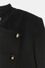 Vestido tipo blazer de corte estructurado, color negro, con cuello subido y cierre frontal cruzado con botones metálicos dorados. Presenta mangas largas con trabillas en los puños y bolsillos de vivo decorativos en el frente.