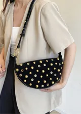 Bolso pequeño de hombro con forma de media luna, color negro, decorado con tachas redondas doradas. Cuenta con una correa ajustable y herrajes dorados.