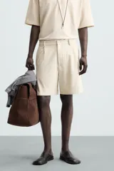 Bermuda de hombre color verde claro, de corte regular y tiro medio, con pinzas frontales, bolsillos laterales y bolsillos traseros de vivo. Cierre frontal con botón y cremallera.