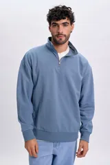 Buzo deportivo color azul piedra, con cuello alto, cierre frontal parcial y mangas largas con puños elásticos.