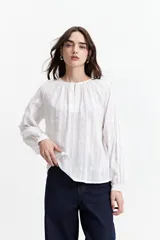 Blusa de manga larga color negro, confeccionada en 100% algodón con textura bordada. Presenta detalles de tablas en el frente y en los puños, con un corte holgado y cuello redondo con pequeña abertura.