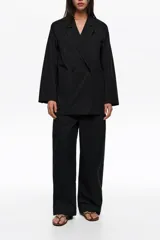 Chaquetón sastrero negro de doble botonadura en mezcla de algodón y poliamida, con solapas de muesca, mangas largas, bolsillos frontales de parche y pespuntes decorativos.
