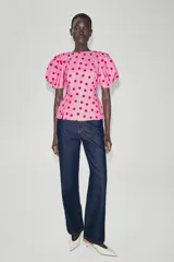 Top rosado con estampado de lunares fucsia, de cuello redondo y mangas cortas abullonadas con pliegues. Cuenta con escote en V en la espalda y cierre con cremallera oculta.