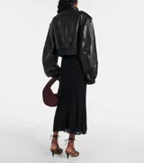 Campera bomber corta de cuero sintético negro, con cuello alto, cierre frontal y detalles de botones metálicos plateados en hombros y bolsillos frontales.