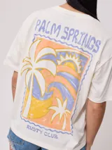 Remera color salmón de corte holgado, con estampado pequeño en el frente que incluye un arcoíris y el texto "Rusty Club".