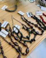 Conjunto de collares de cuentas de diferentes colores y materiales, incluyendo cuentas de piedra, madera y cristal. Los collares tienen cadenas doradas y etiquetas blancas con la marca "MANDRA".