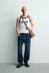 Camiseta sin mangas slim fit color blanco, con cuello redondo y sisas ribeteadas en azul marino. Estampado frontal con la palabra "League" y el número "'86" en azul marino.