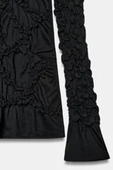 Top negro de cuello perkins y manga larga con frunces en el pecho y las mangas.