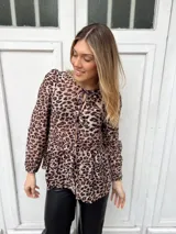 Blusa marrón con estampado animal print, escote redondo con lazo ajustable, mangas largas con puños elásticos y corte peplum.