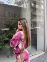 Conjunto de dos piezas compuesto por un buzo corto de manga larga y un pantalón de pierna ancha, confeccionado en tela morley elastizada con estampado tie-dye en tonos fucsia y marrón.