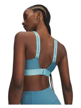 Top deportivo de alto impacto Under Armour, color azul petróleo con detalles en celeste. Presenta diseño con almohadillas moldeadas, paneles de malla para ventilación, tirantes ajustables con logo de la marca y banda elástica inferior con logo Under Armour.