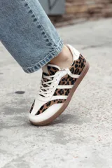 Zapatillas de estilo retro con diseño de paneles, combinando cuero beige con estampado animal print de leopardo y detalles en blanco. Presentan suela de goma color caramelo y cierre con cordones.
