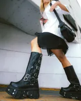 Bota de caña media de cuero negro con plataforma track y múltiples hebillas metálicas.